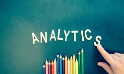 Colored pencils and letters spelling 'ANALYTICS' on a textured background with a hand.